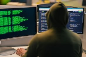 Hacker in hoodie working on multiple computer screens